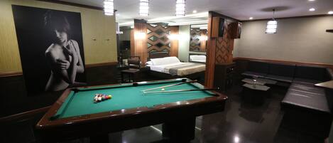 A pool table in a room with a bed, a sofa, and a mirror.