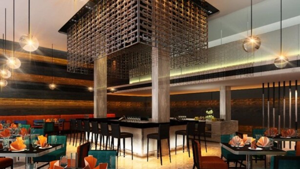 Un restaurant moderne avec un plafond haut, des luminaires suspendus et un bar central.