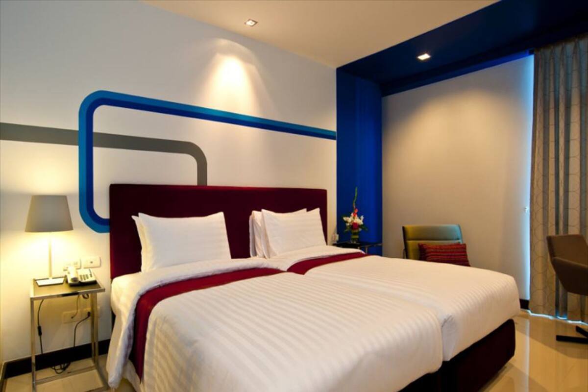 A modern hotel room with a large bed, a nightstand with a lamp, and a chair.