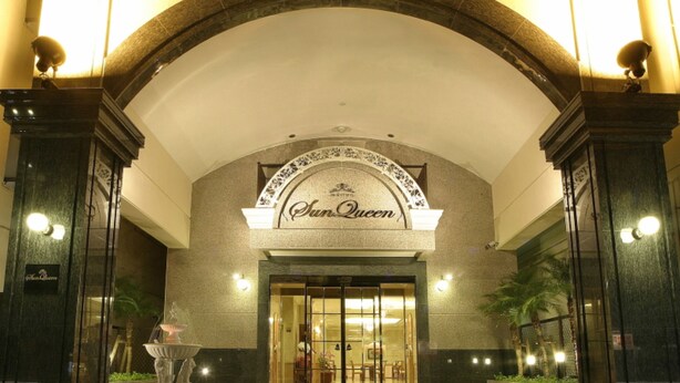 L'ingresso dell'hotel Sun Queen con un'imponente porta ad arco, un cartello sopra l'ingresso e una facciata ben illuminata.