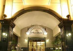 L’entrée de l’hôtel Sun Queen se distingue par son imposante porte en arc de cercle, une enseigne au-dessus de l’entrée et une façade bien éclairée.