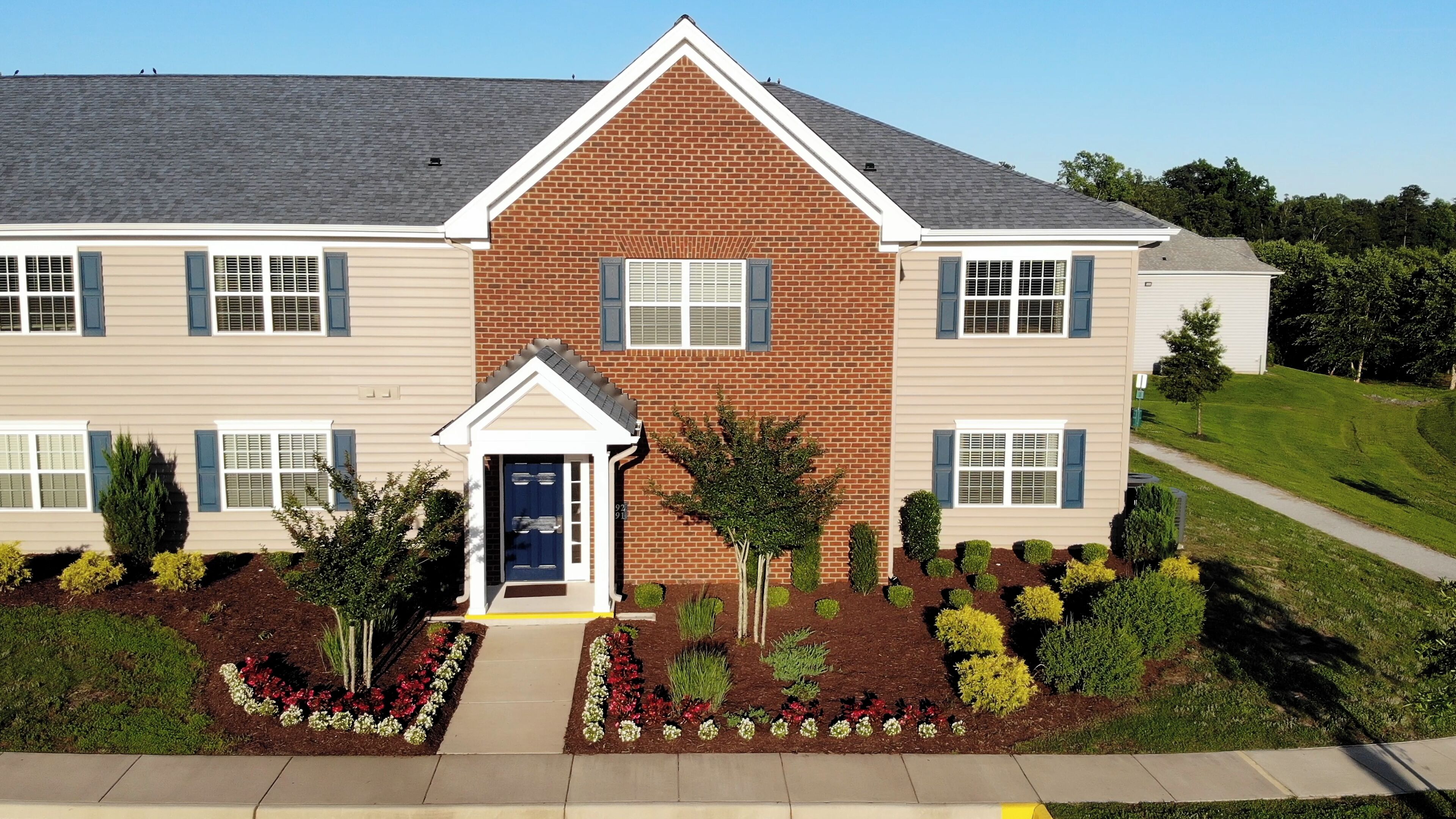 A two-story building with a brick facade, multiple windows with shutters, and a well-maintained garden with various shrubs and flowers.