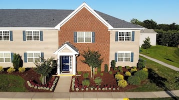 A two-story building with a brick facade, multiple windows with shutters, and a well-maintained garden with various shrubs and flowers.