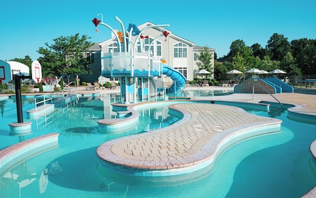 A swimming pool with a water slide, lounge chairs, and a basketball hoop.