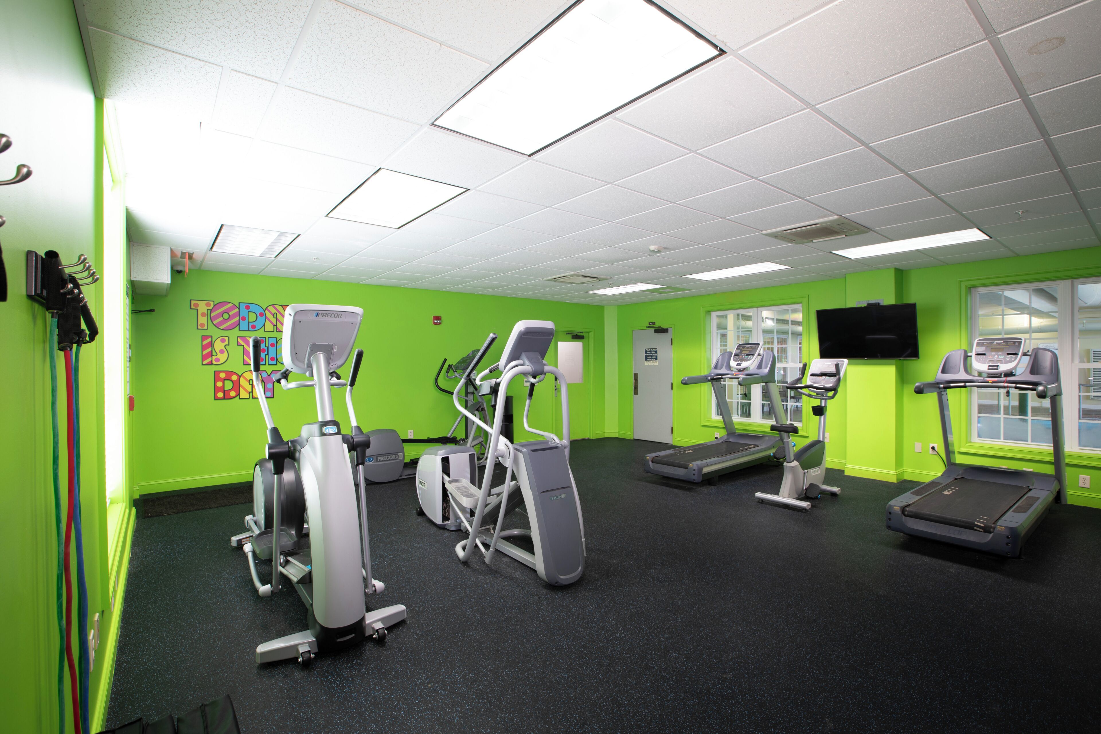 A gym with various exercise equipment, green walls, and a television on the wall.