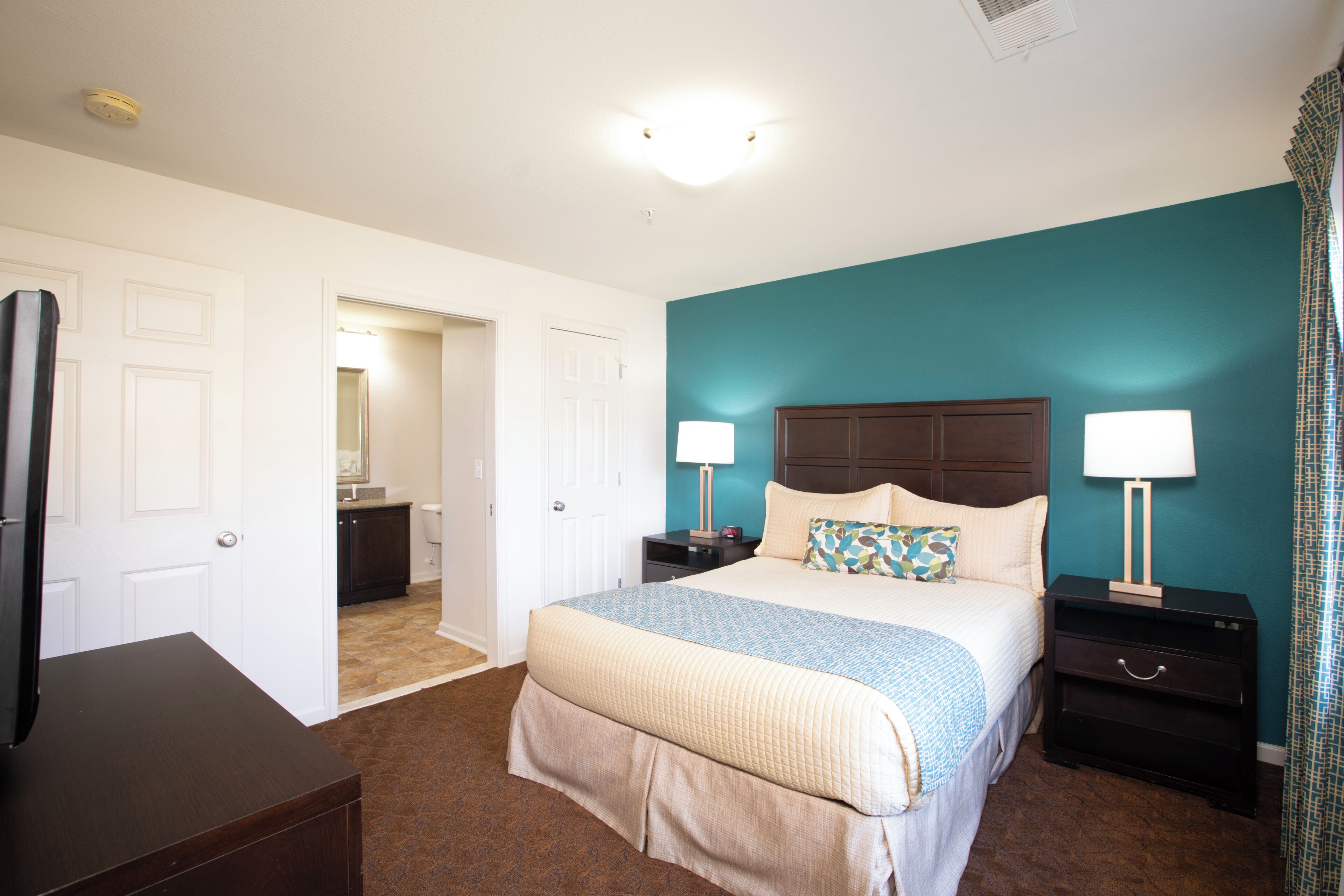 A bedroom with a bed, nightstands, a dresser, and a television.