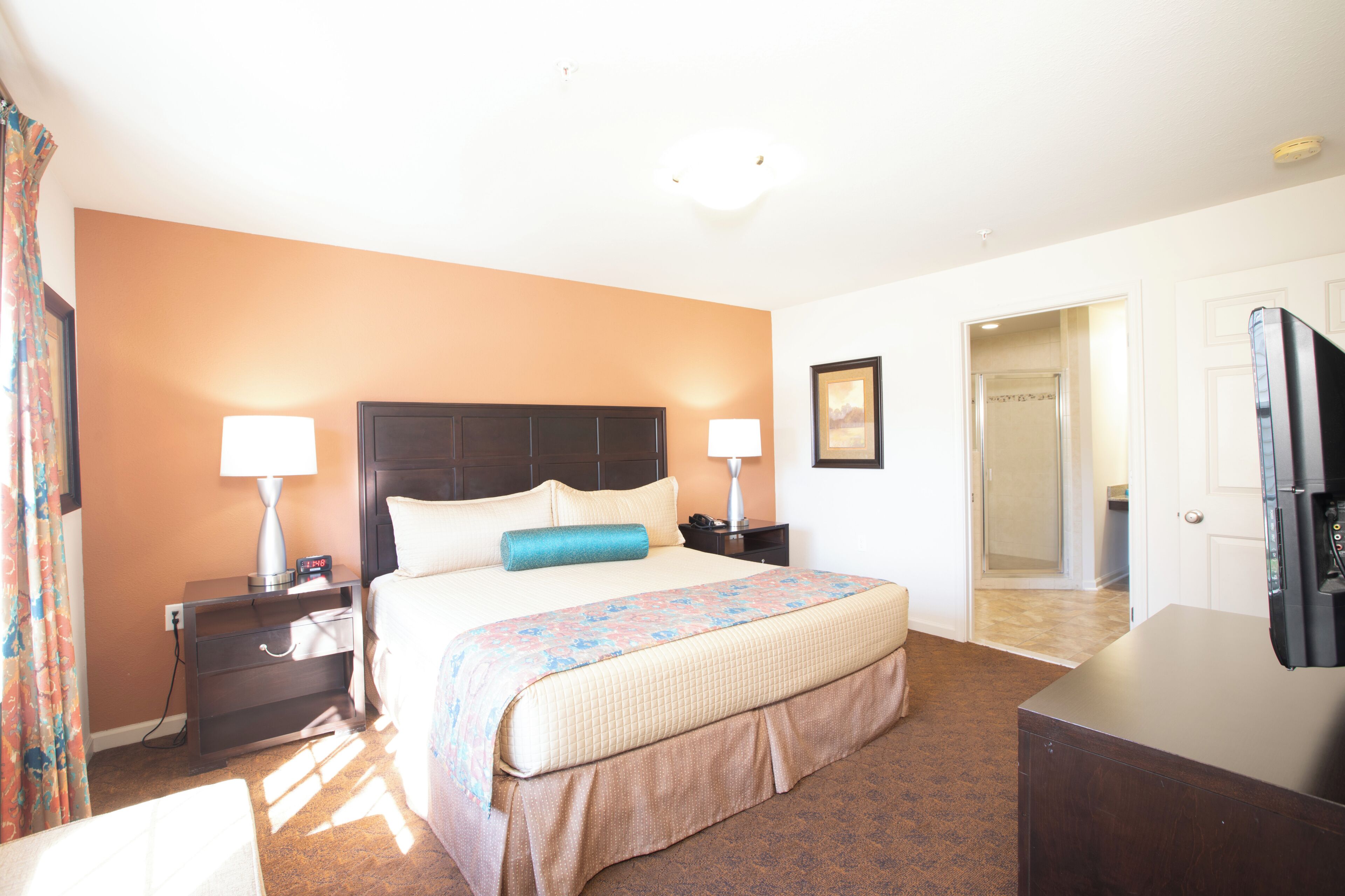 A hotel room with a bed, two bedside tables with lamps, a dresser, and a television.