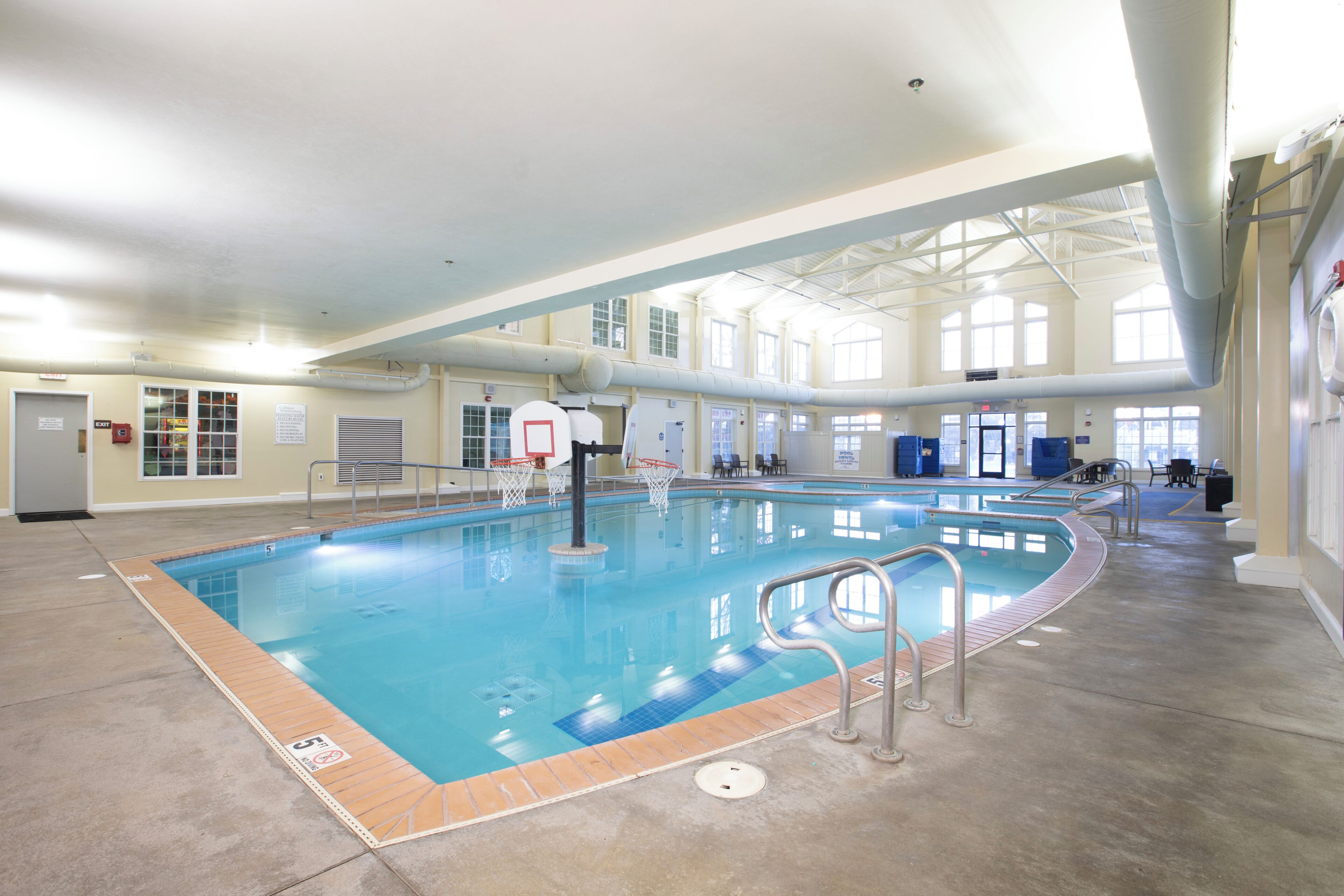 An indoor swimming pool with a basketball hoop, clear ceiling, and large windows.
