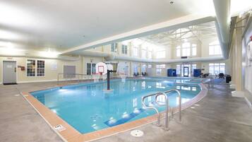 An indoor swimming pool with a basketball hoop, clear ceiling, and large windows.