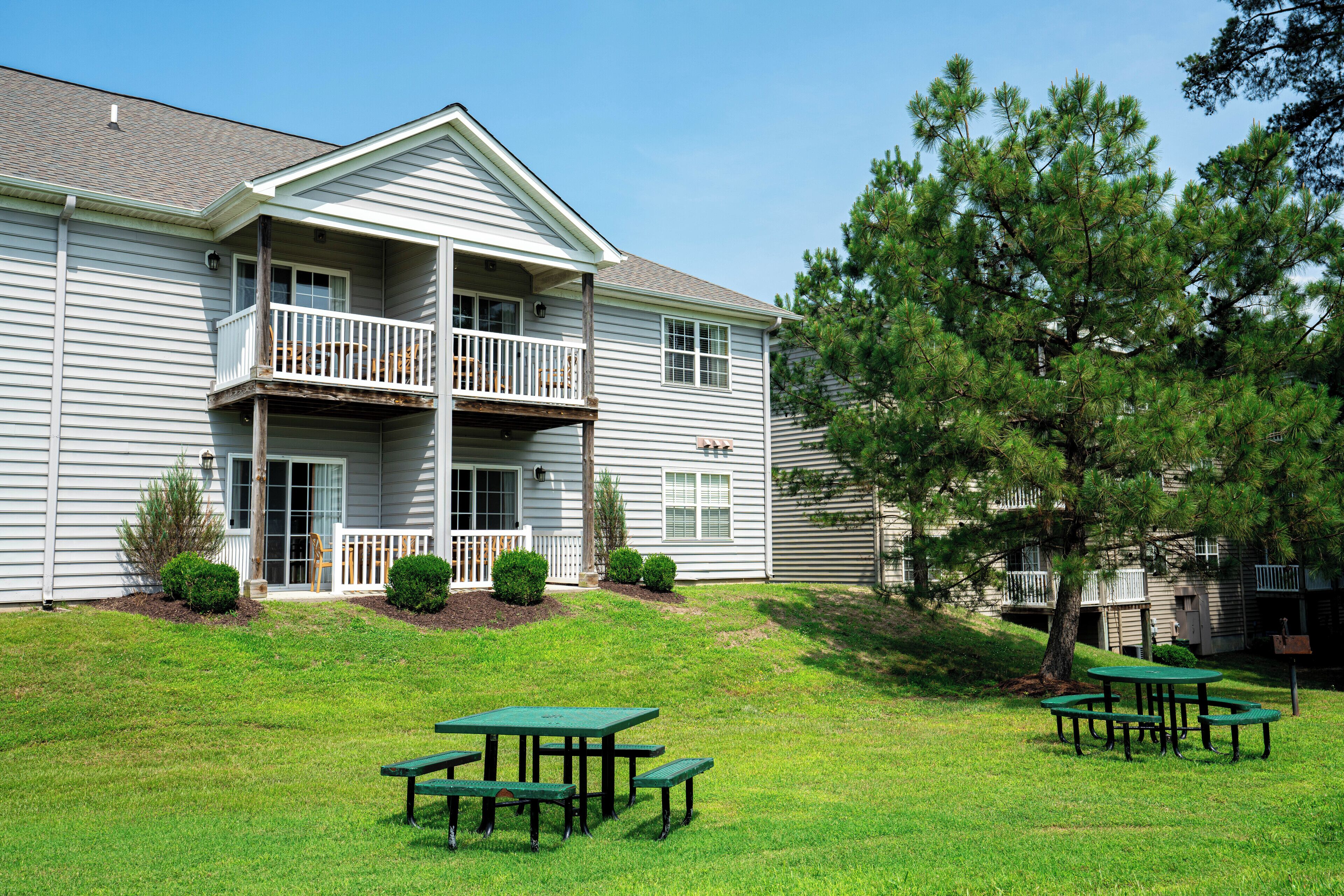 A two-story building with a balcony, a grassy lawn, and picnic tables.