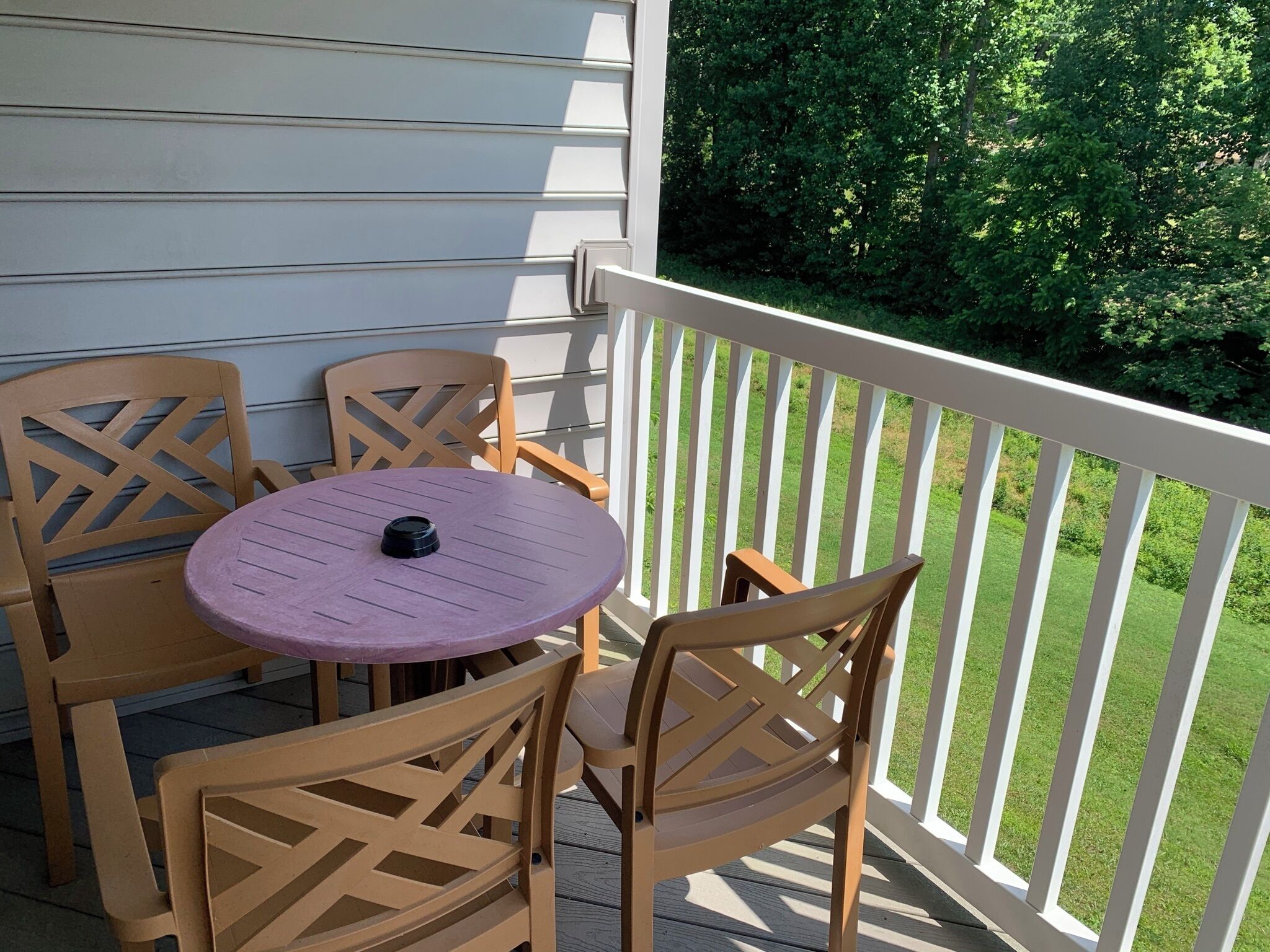 Un balcon avec une table ronde et deux chaises, une balustrade blanche et une vue sur la verdure.