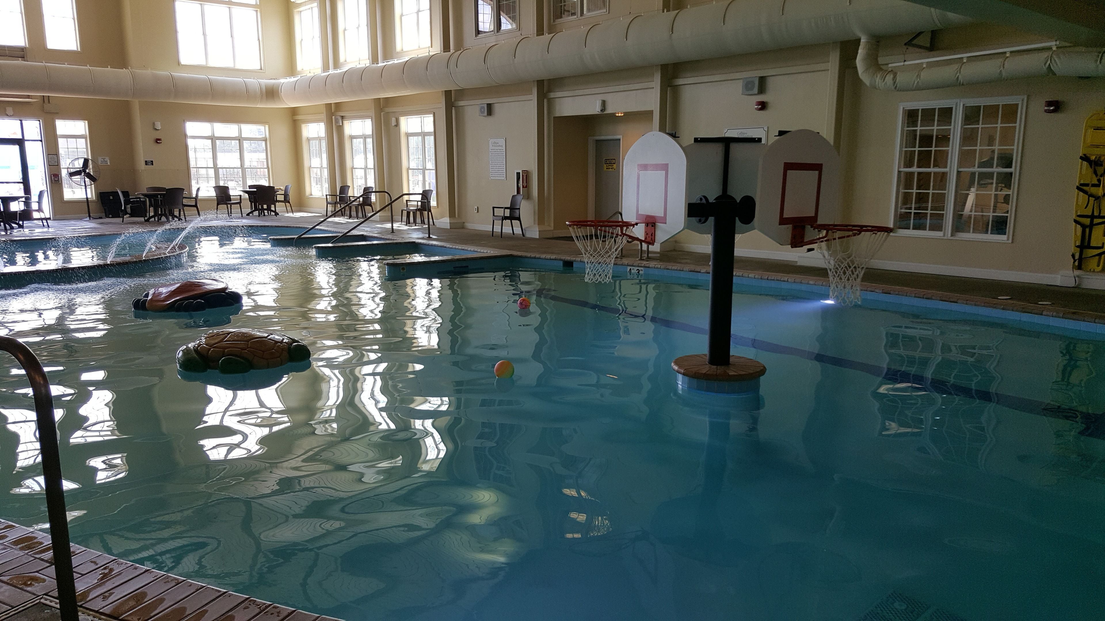 Una piscina interior amb un cèrcol de bàsquet, un trampolí i una zona de fusta.