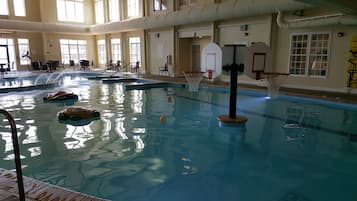 Una piscina interior amb un cèrcol de bàsquet, un trampolí i una zona de fusta.