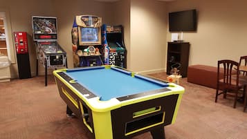 A pool table in a room with arcade games, a television, and a seating area.