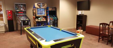 A pool table in a room with arcade games, a television, and a seating area.