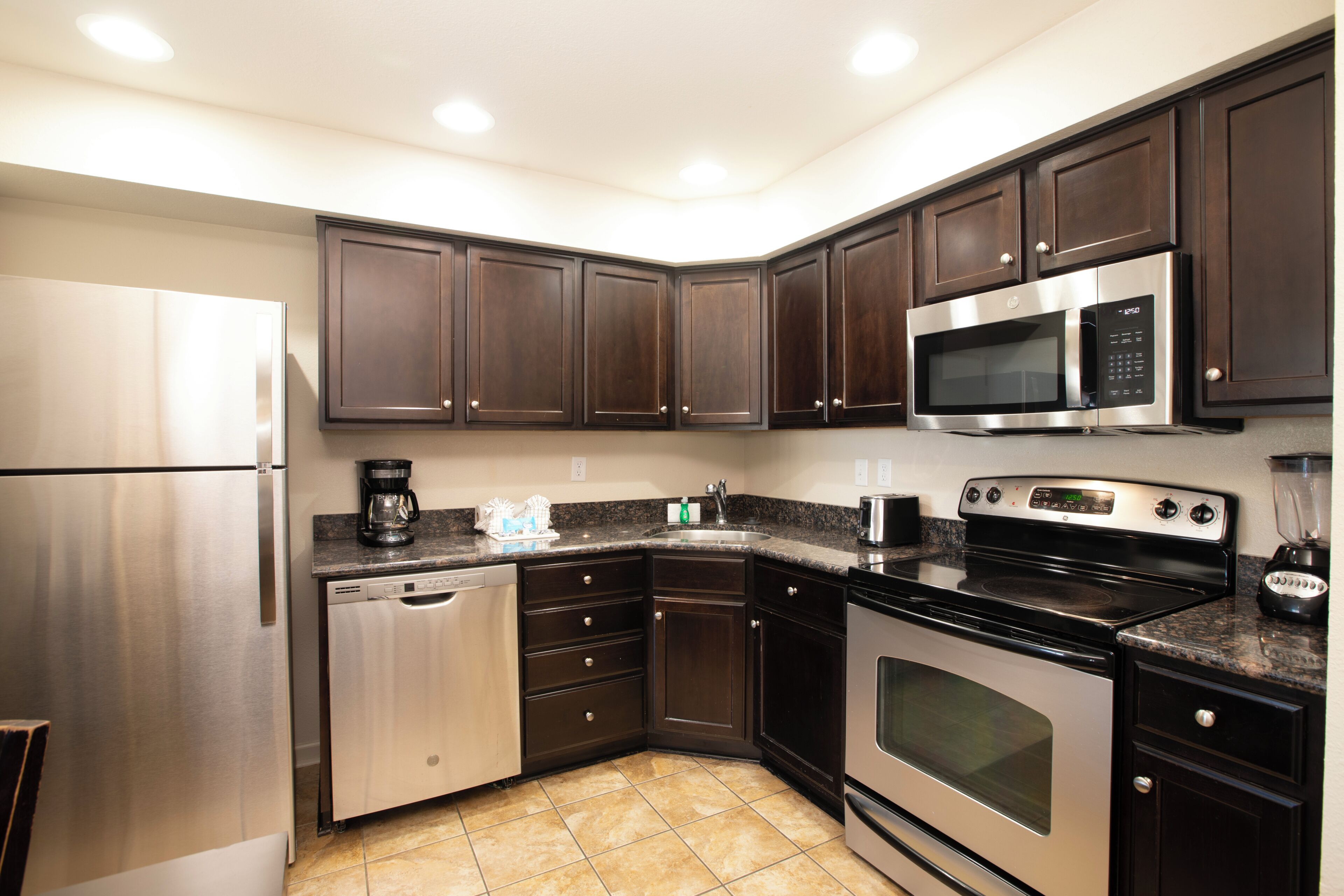 A modern kitchen with stainless steel appliances, dark wood cabinets, and a granite countertop.