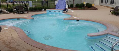Una piscina con un letrero que indica ‘no saltos’ de casi un metro, una zona cubierta y un patio vallado con sillas y mesas.