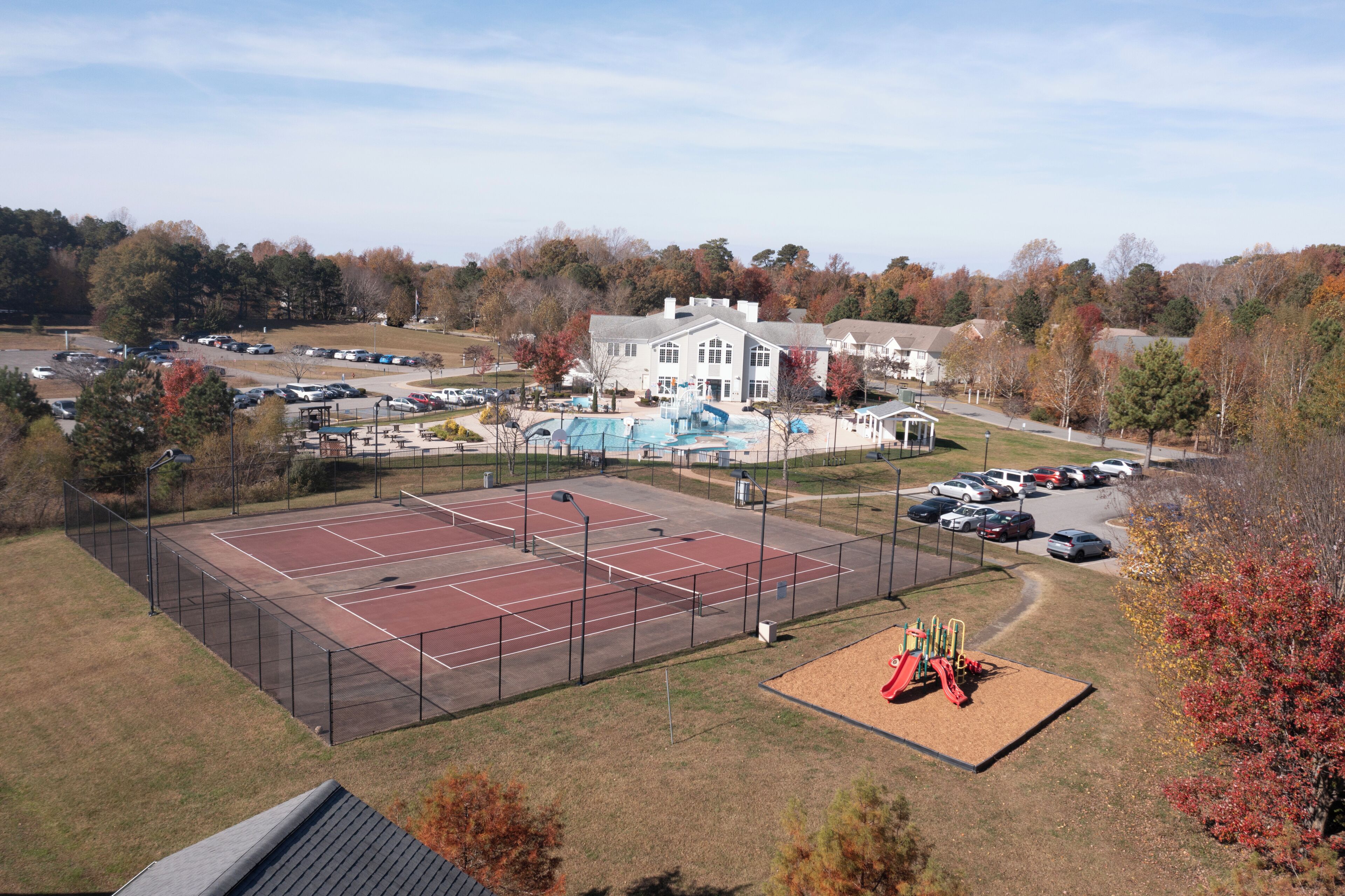 A tennis court, playground, and a large building with a parking lot.