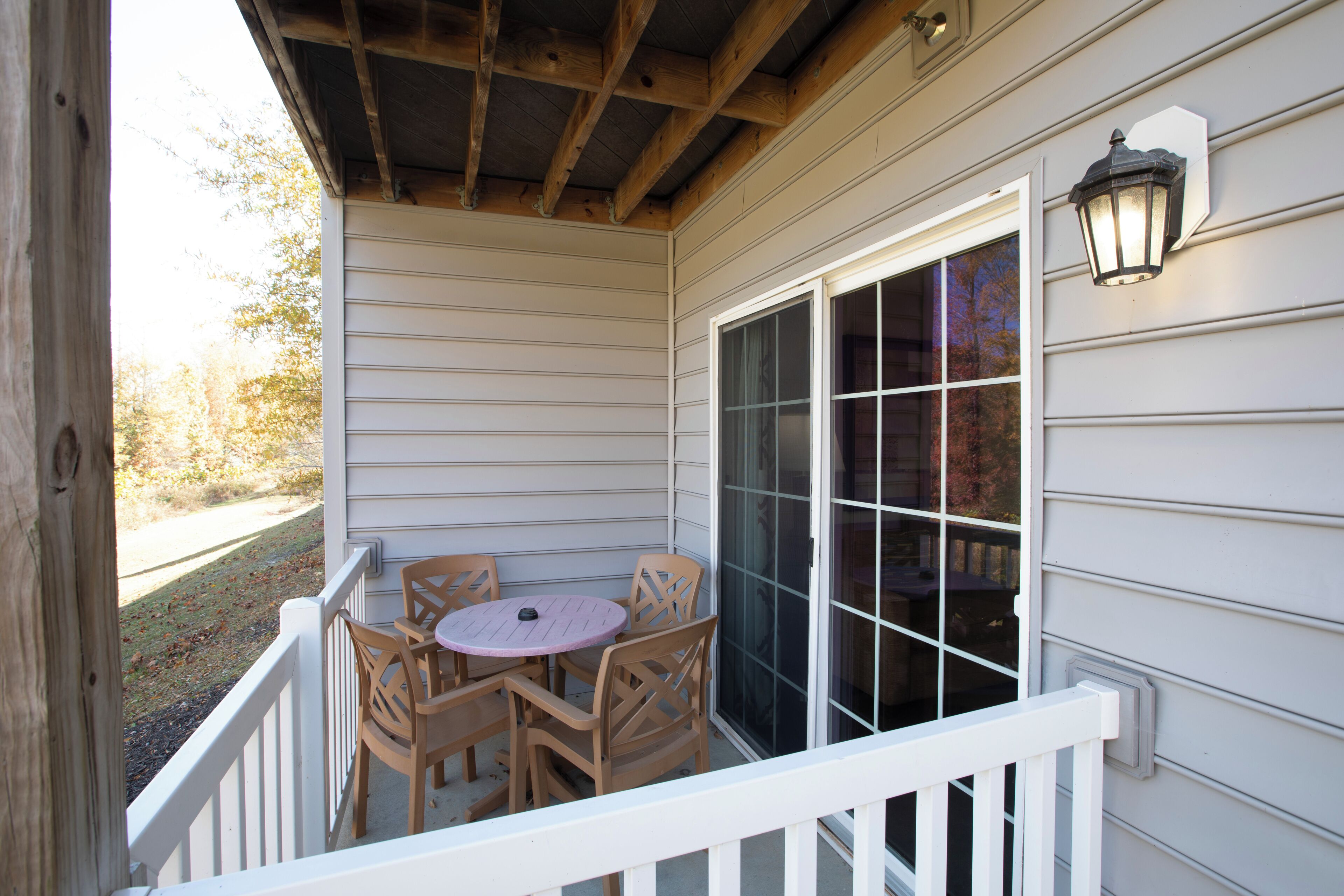 A covered porch with a table and chairs, a window, and a wall-mounted light fixture.