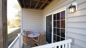 A covered porch with a table and chairs, a window, and a wall-mounted light fixture.