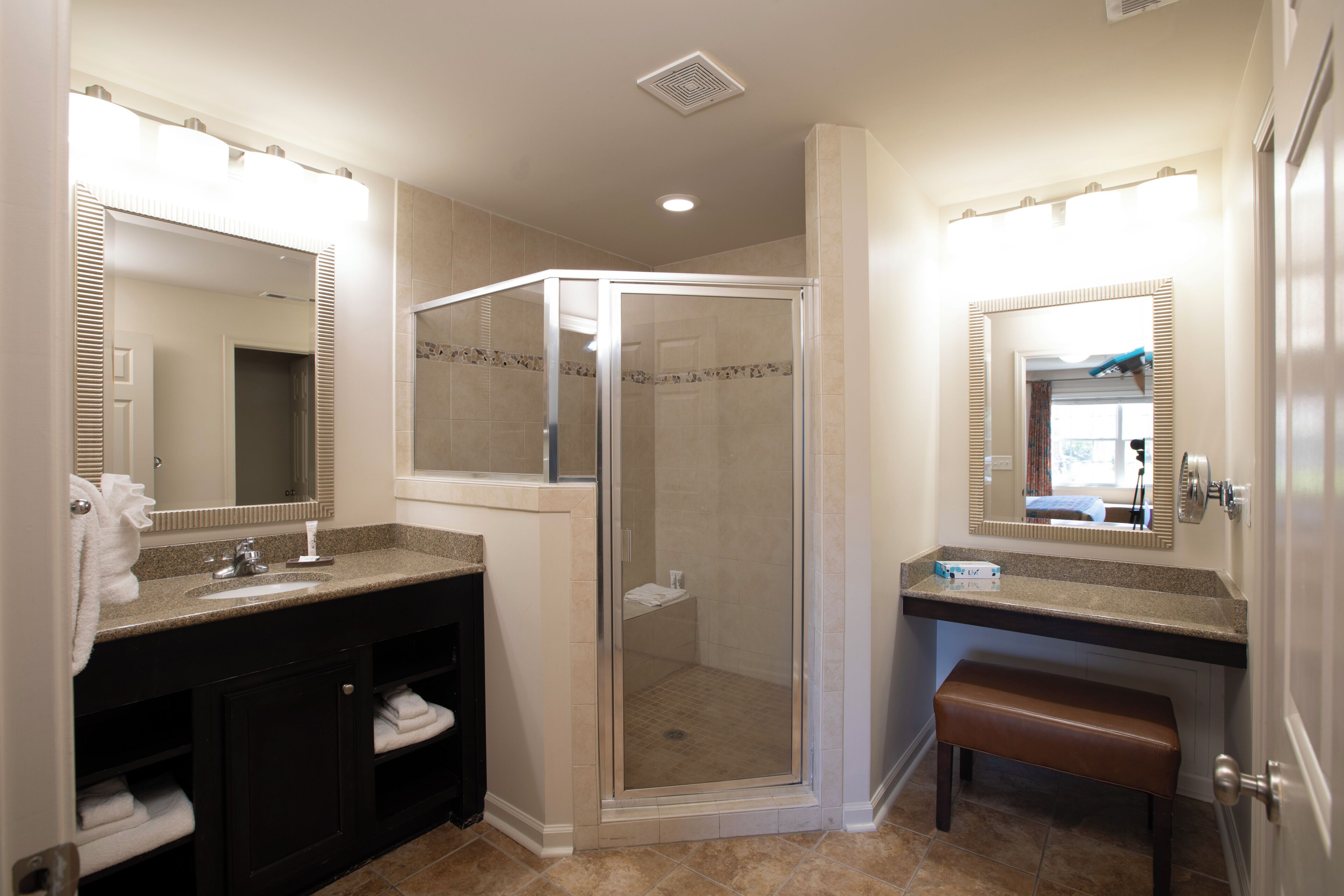A bathroom with a shower, sink, vanity, and a bench.