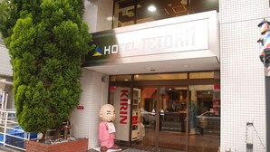 Entrada de hotel com uma árvore grande, uma estátua e uma placa com a inscrição "HOTEL TETORO".