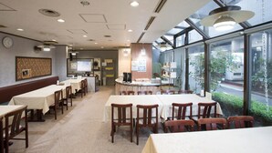 Restaurante com várias mesas e cadeiras, um balcão com menu e grandes janelas que oferecem vista para a rua.