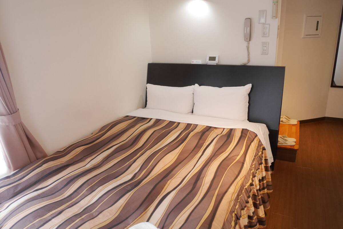 Ett hotellrum med en säng, ett nattduksbord med en telefon och en väggmonterad termostat.