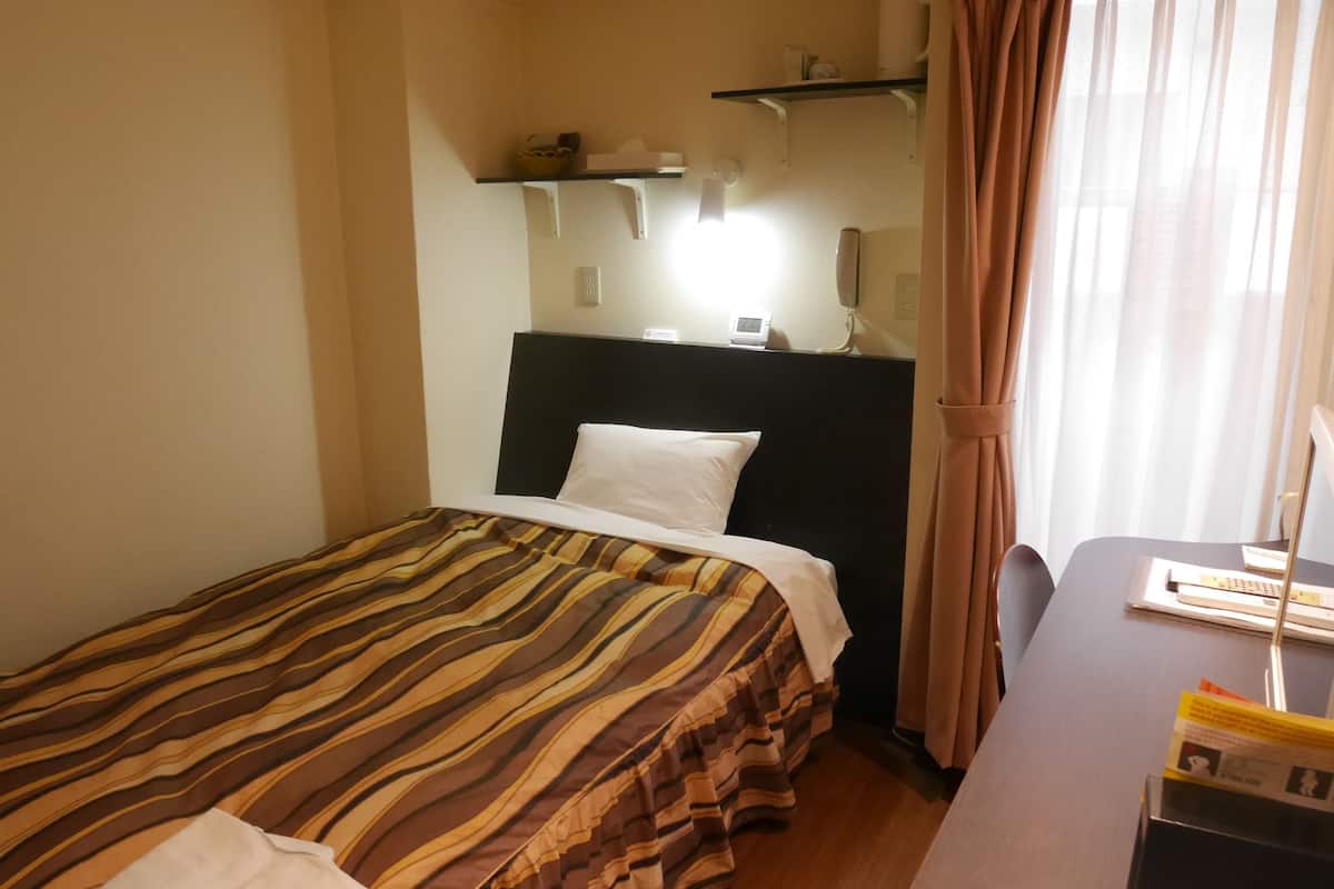 Ett hotellrum med en säng, ett skrivbord och ett fönster med gardiner.