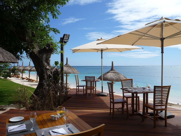 A wooden deck with tables and chairs, umbrellas, and a view of the ocean.