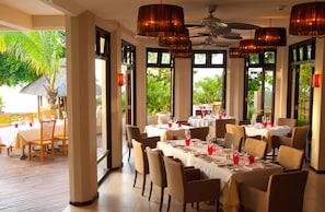 A restaurant with multiple tables set for dining, large windows, and a ceiling fan.