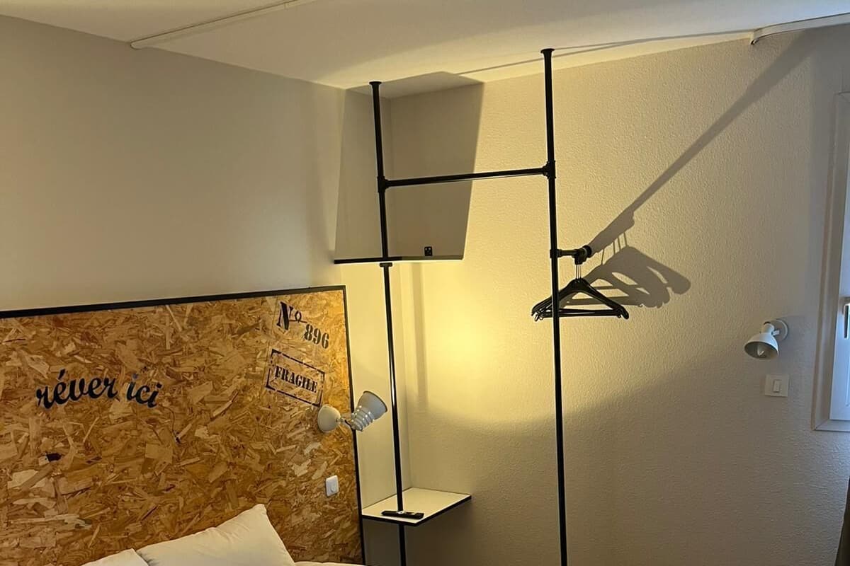 A neatly made bed with a black headboard, a bedside table, a wall-mounted lamp, and a small shelf.