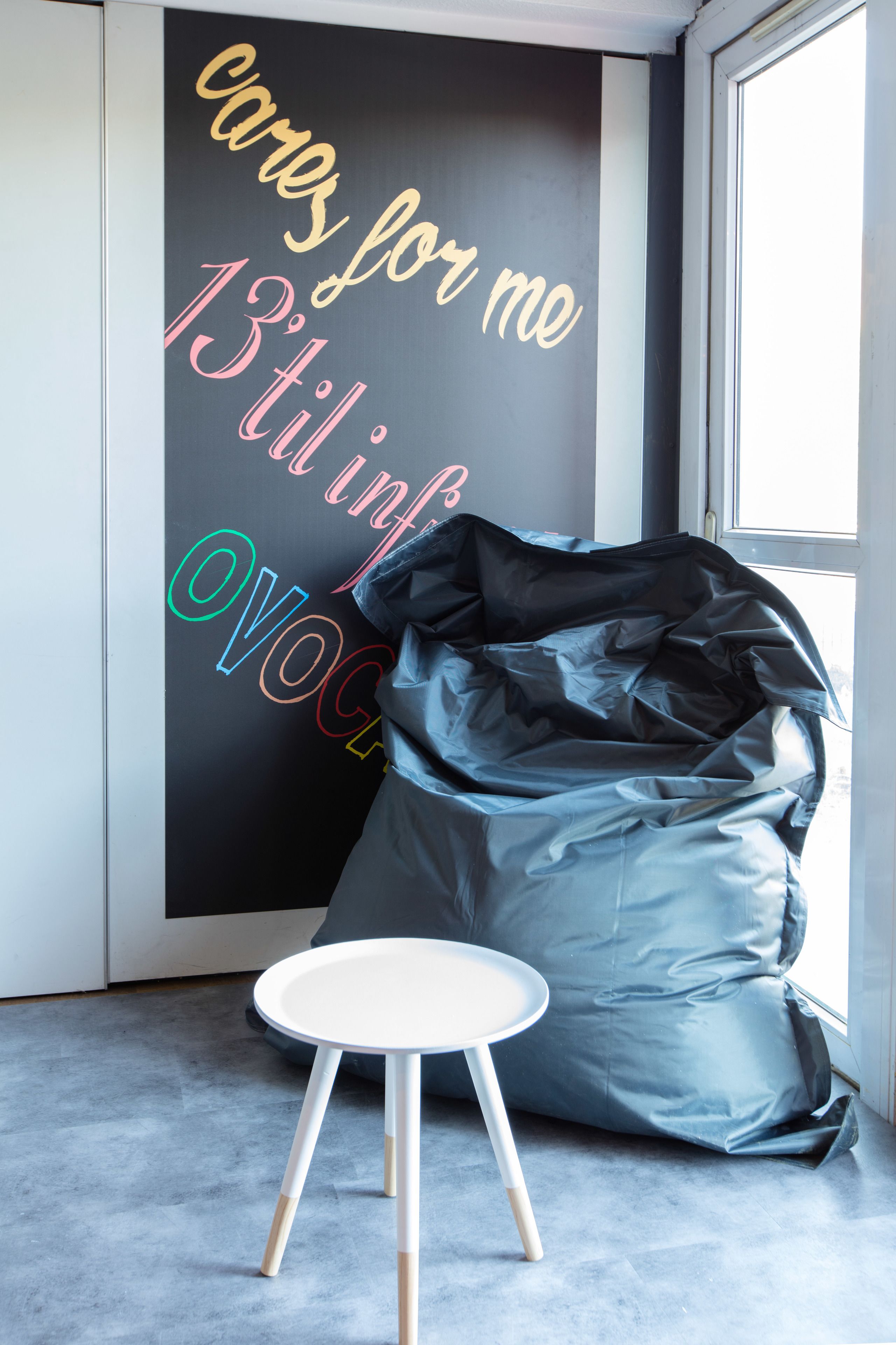 Una habitación con un muro de pizarra con texto de colores, un sillón informal gris y una pequeña mesa blanca.