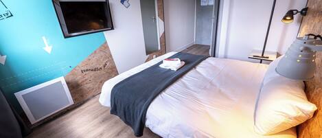 A modern hotel room with a bed, a TV, a desk, and a lamp.