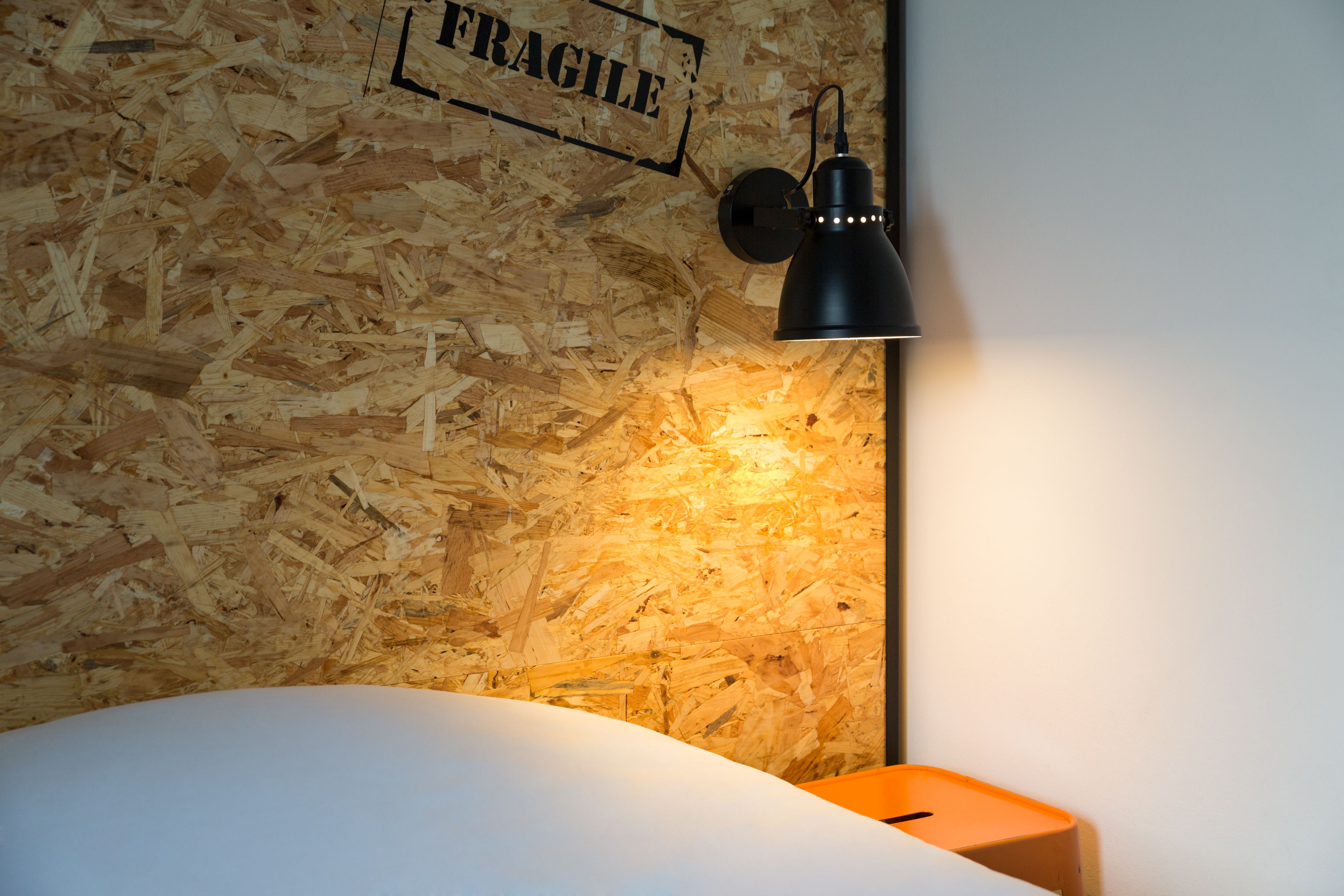 A room with a wooden wall, a black lamp, and a bed.