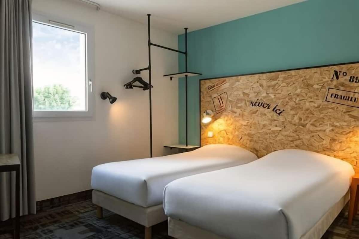 A room with two beds, a window, a wall-mounted light, and a wooden headboard with text.