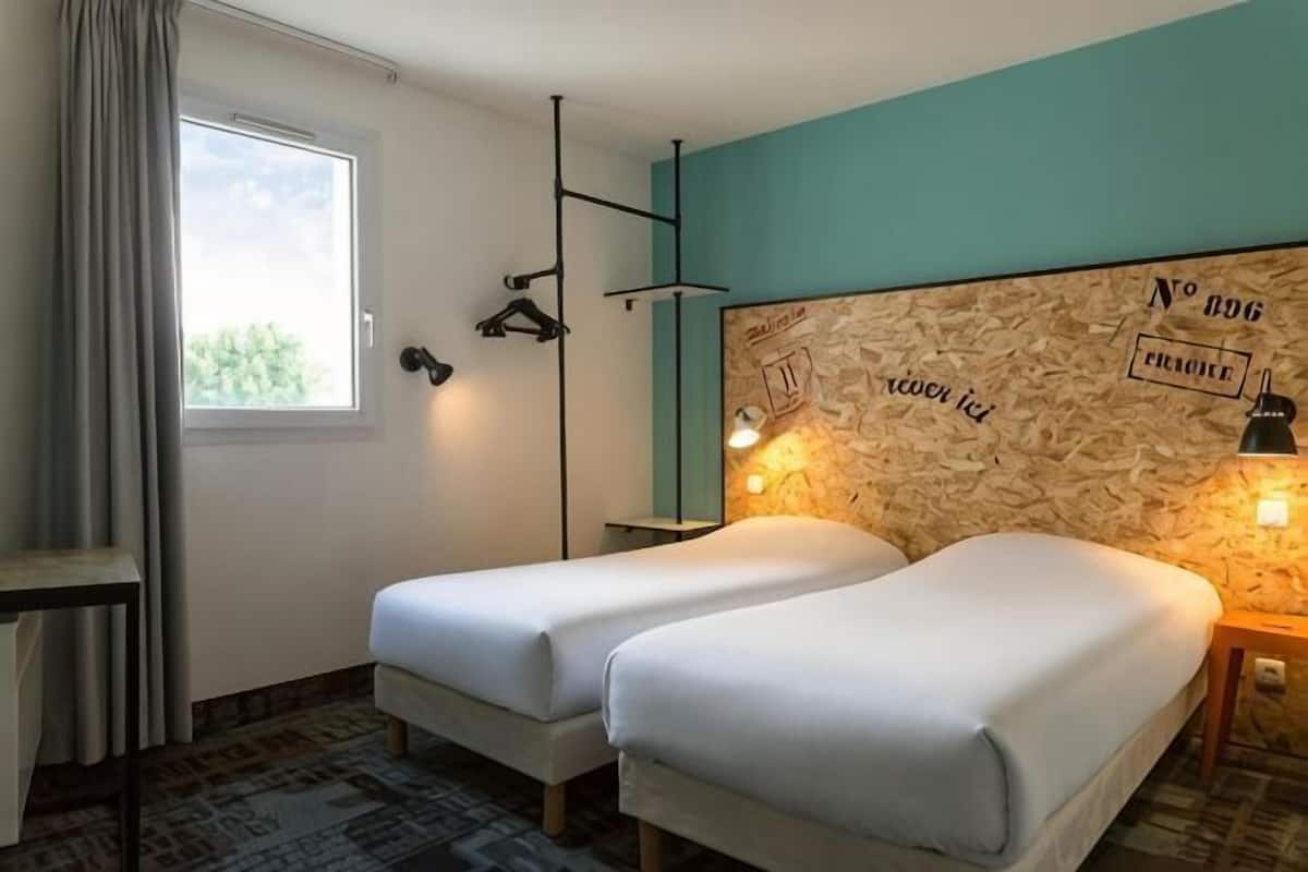 A room with two beds, a window with curtains, a wall-mounted lamp, and a map on the wall.