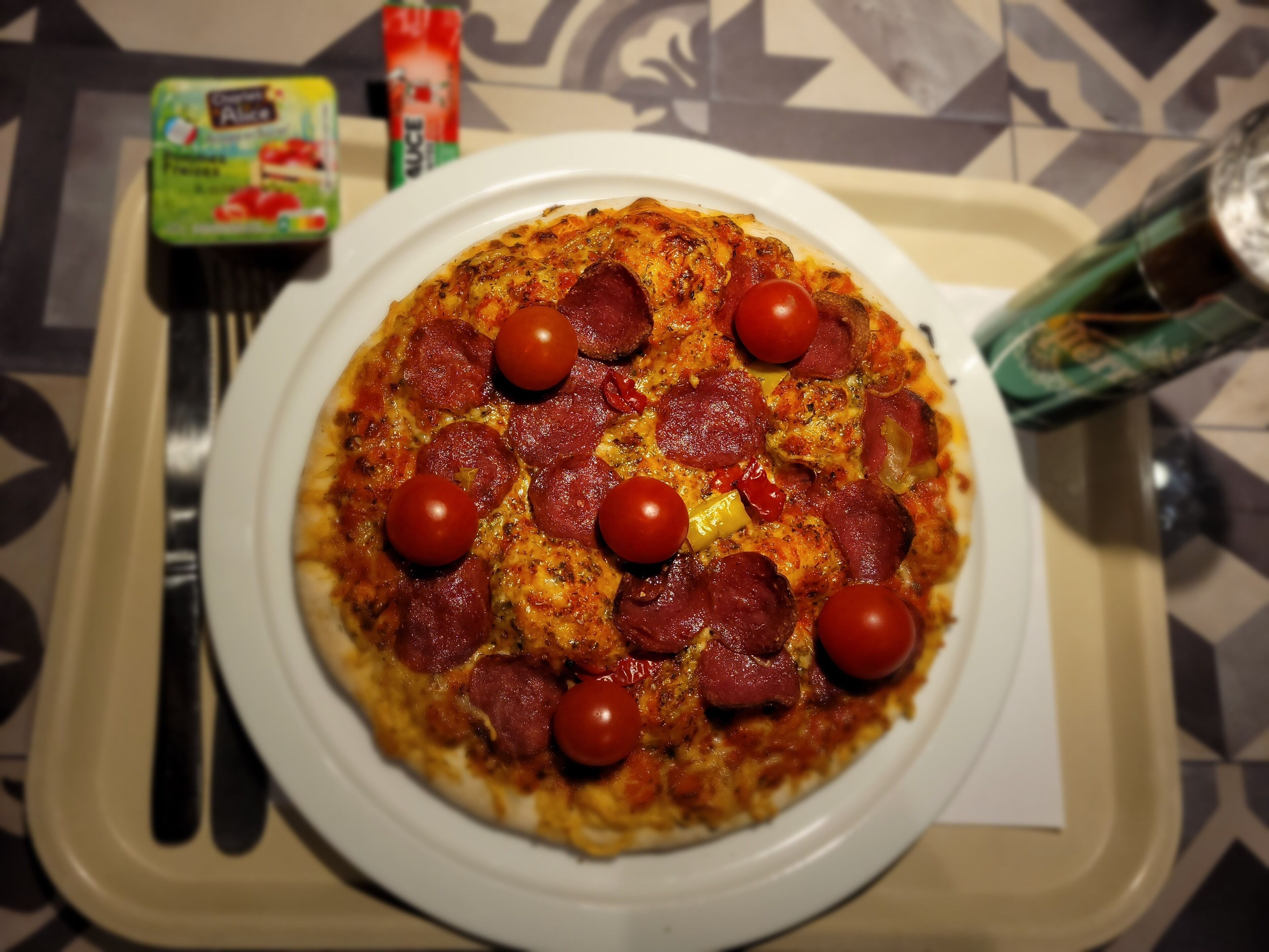 Pizza med pepperoni og kirsebær tomater på en hvid tallerken.