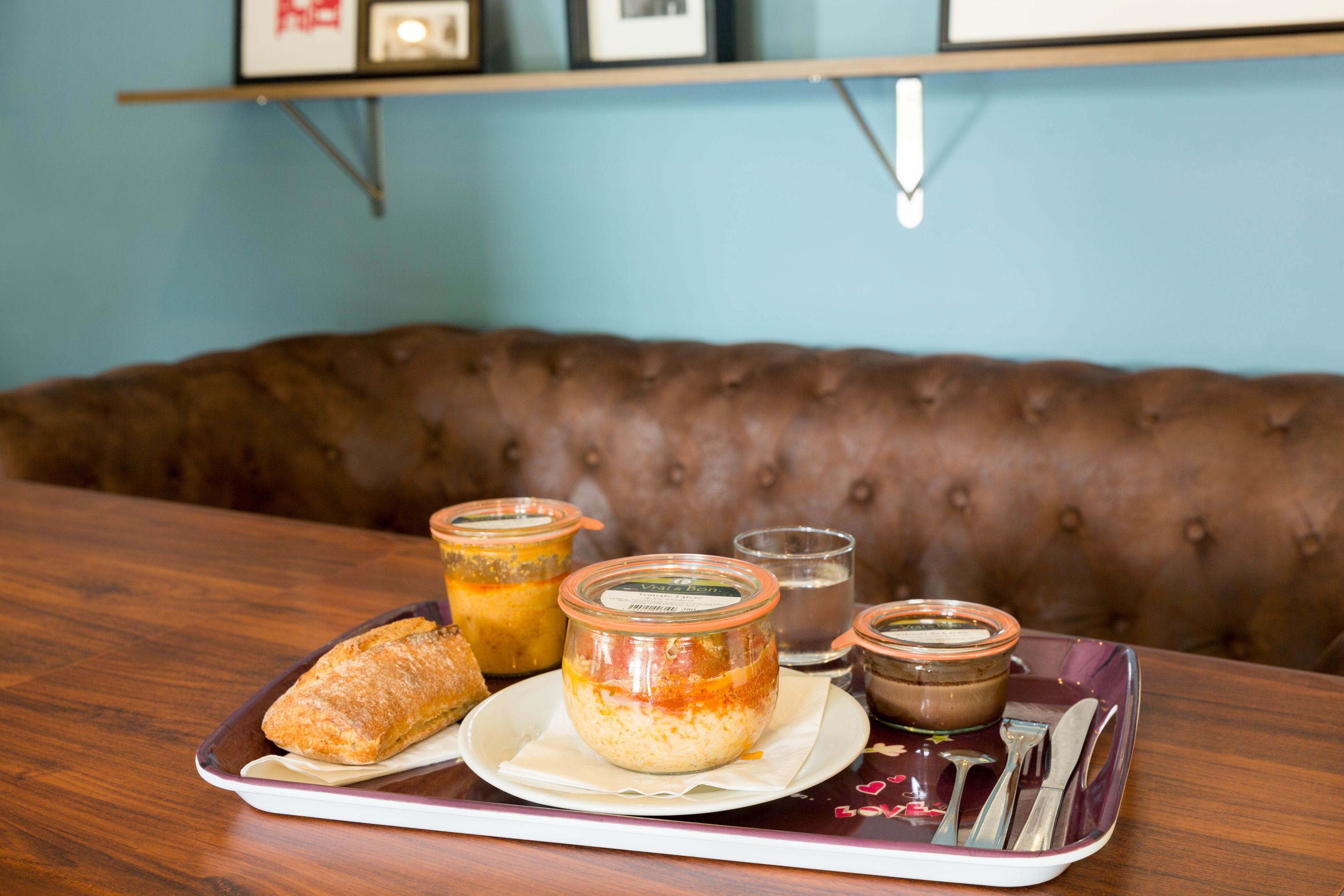 A dining table with a tray containing a pastry, two jars of jam, and a small bowl of soup.
