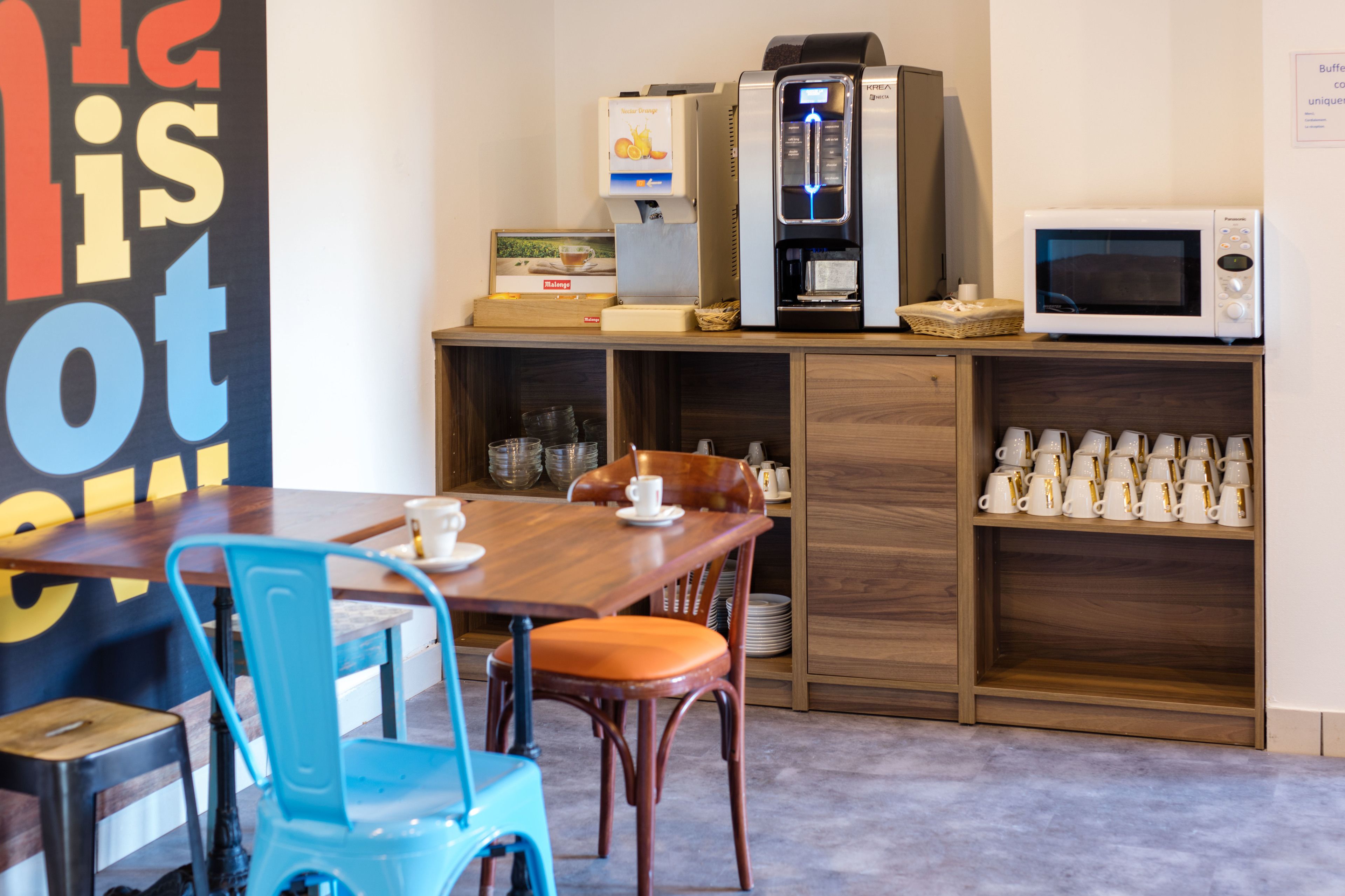 A compact kitchen area with a coffee machine, microwave, and a shelf with cups.