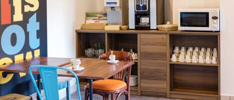 A compact kitchen area with a coffee machine, microwave, and a shelf with cups.