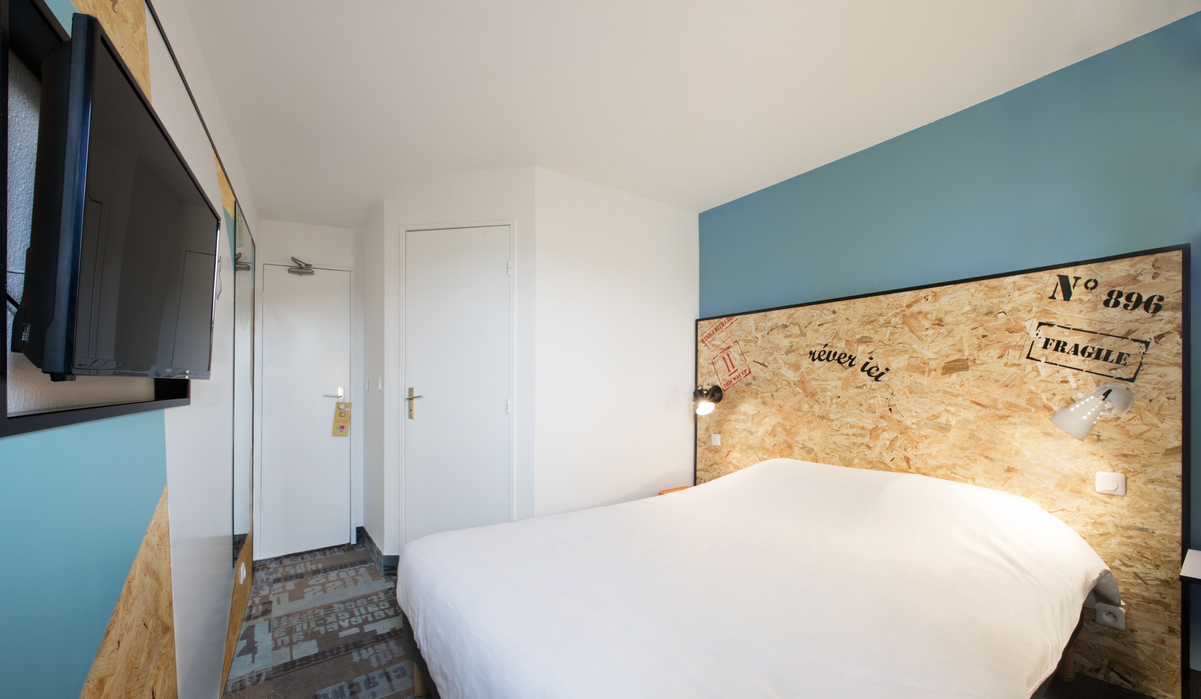 A hotel room with a bed, a television mounted on the wall, and a door leading to another room.