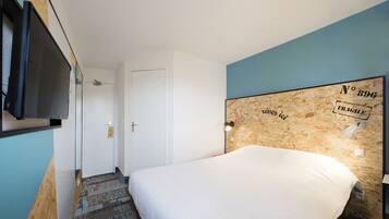 Quarto de hotel com uma cama, televisão fixada na parede e uma porta que dá para outro espaço.