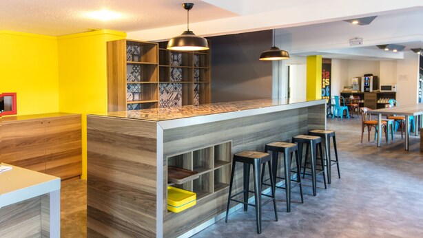 Un área de bar moderna con mostrador de madera, taburetes y lámparas colgantes.