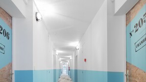 Un largo pasillo de hotel, angosto, con paredes azules y blancas, una alfombra estampada y puertas con números de habitación.
