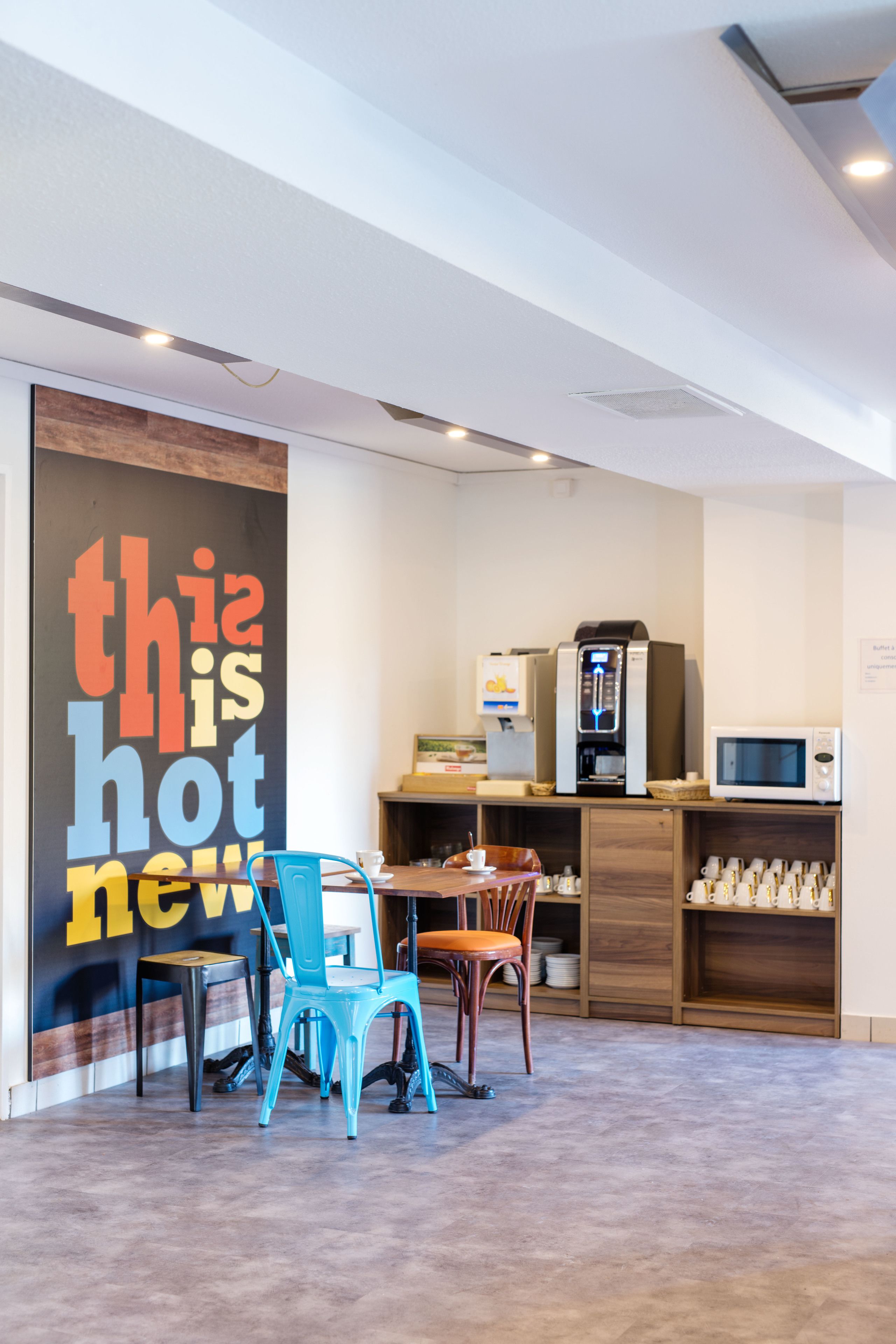 Una cafetería moderna con una máquina de café, zona de estar y una pared grande con texto motivacional.
