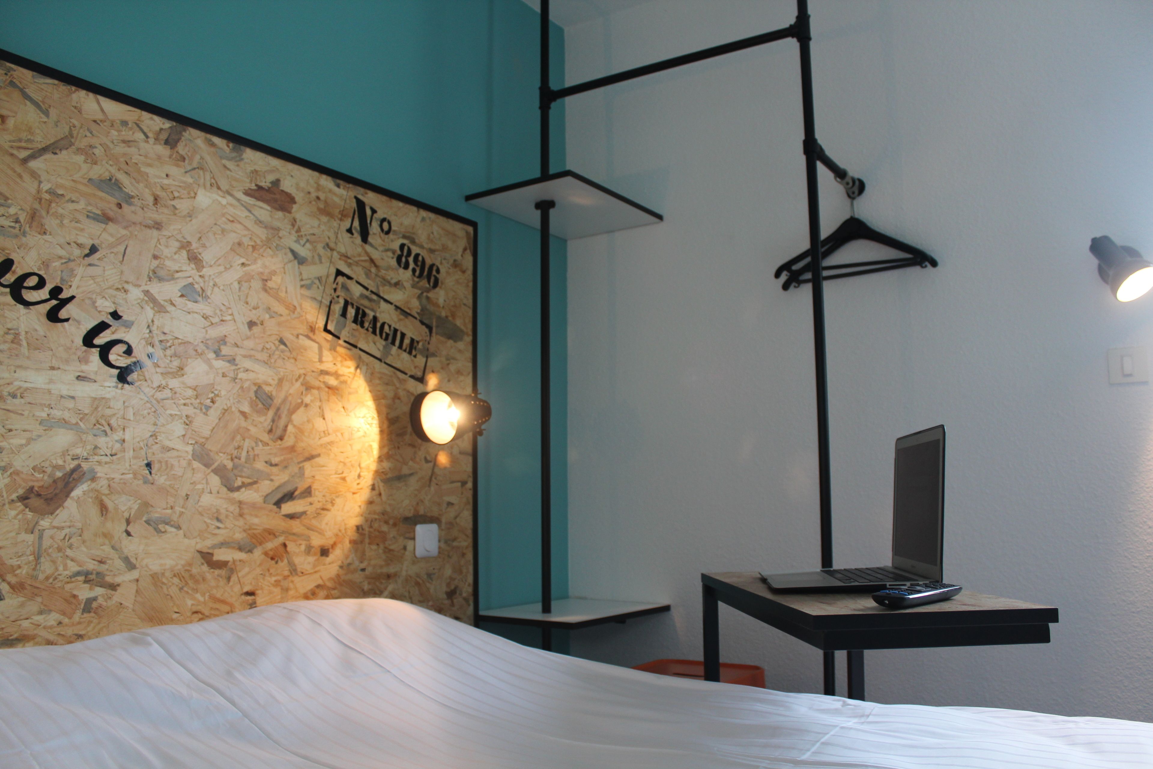 Un dormitorio con una cama, un escritorio con una computadora portátil, una lámpara colgante y una pared con textura de madera.