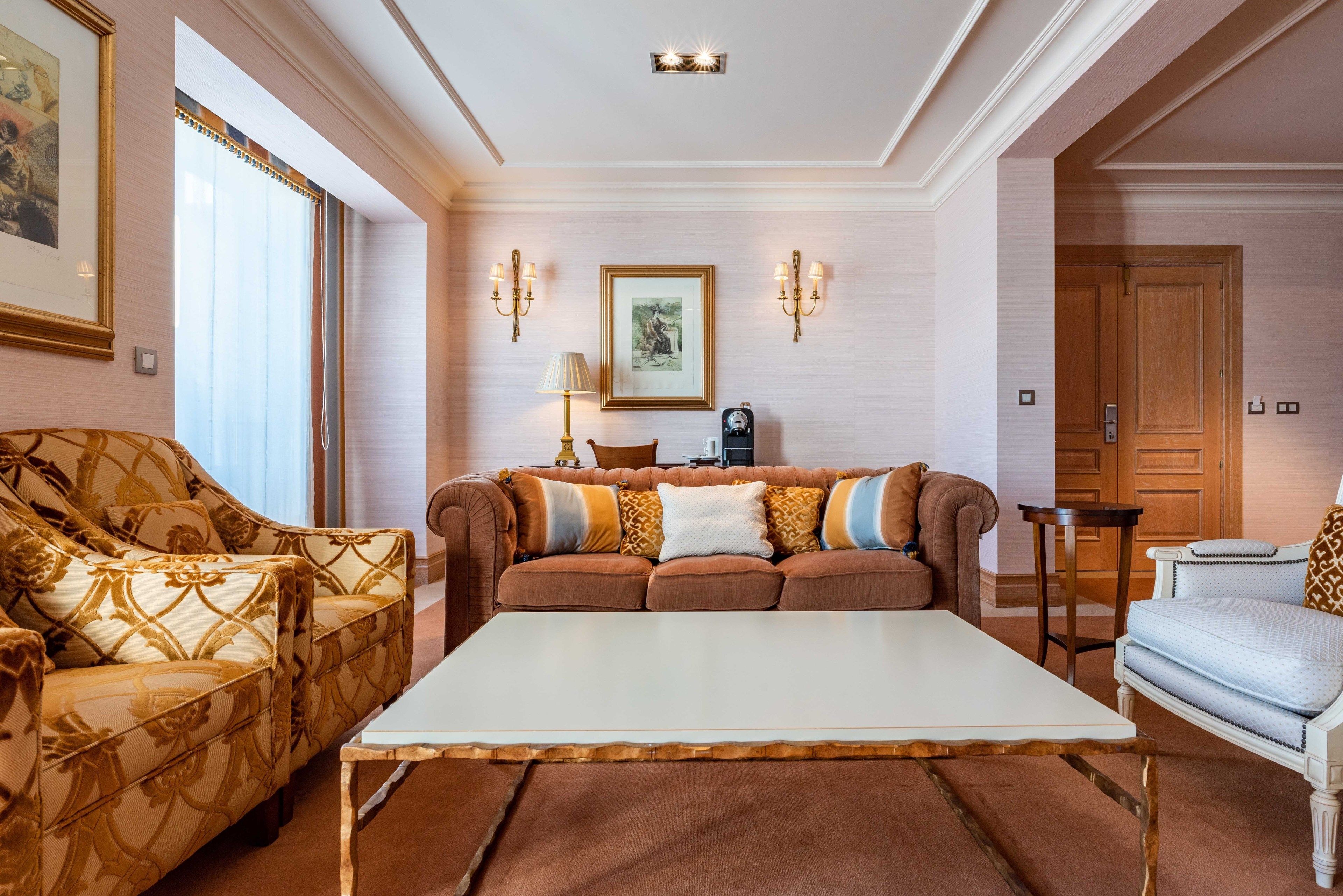 Una sala de estar con un sofá marrón, una mesa de centro blanca y un sillón estampado.