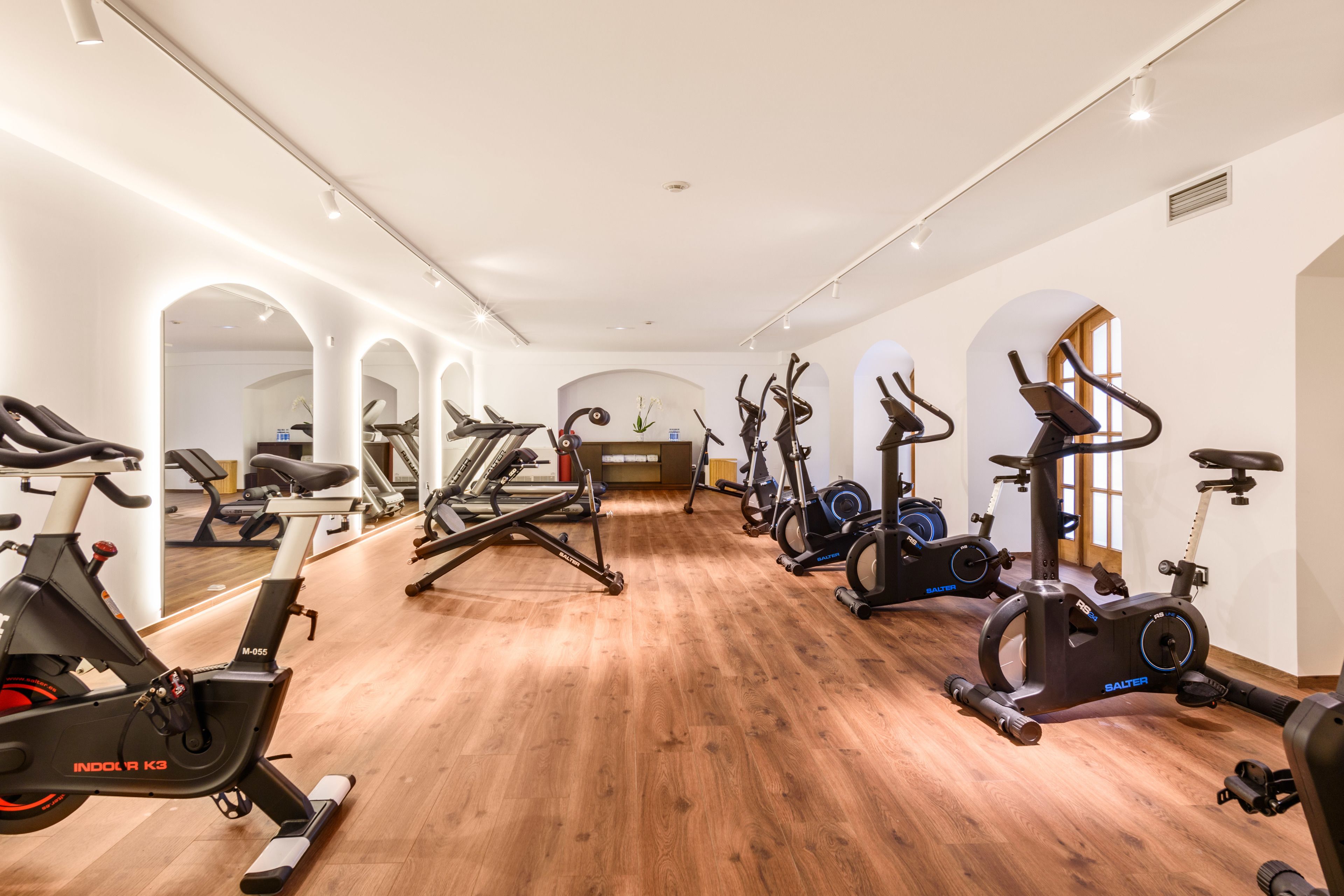 A gym with multiple exercise machines, wooden flooring, and a mirrored wall.