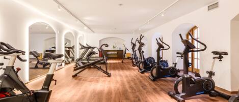 A gym with multiple exercise machines, wooden flooring, and a mirrored wall.
